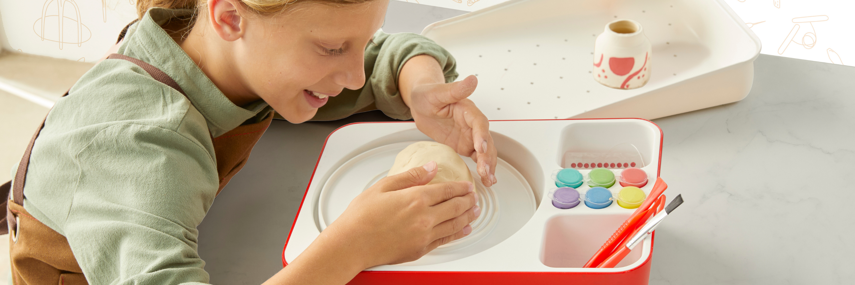 Child playing with colorful play dough in a red container on a light surface.