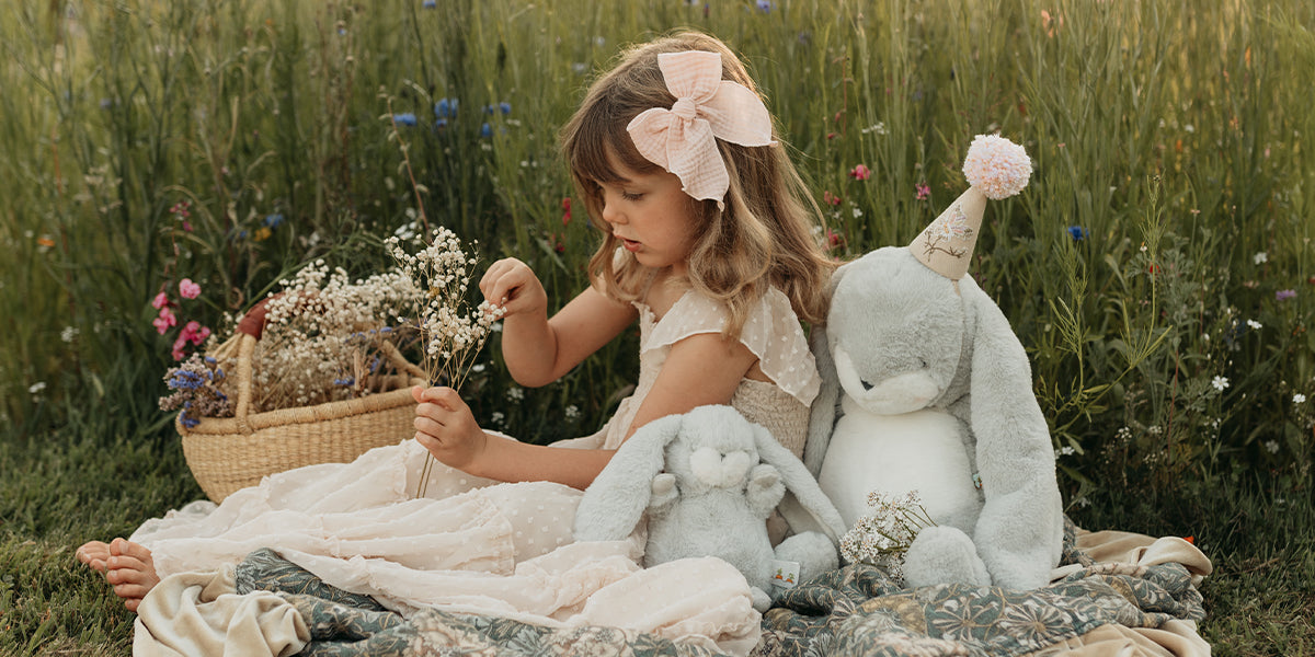 Child sitting in a field with stuffed animals and flowers