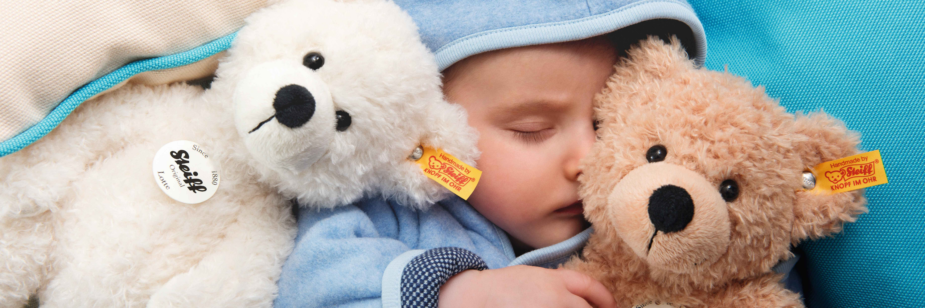 Child sleeping with a white teddy bear and a brown teddy bear on a blue blanket