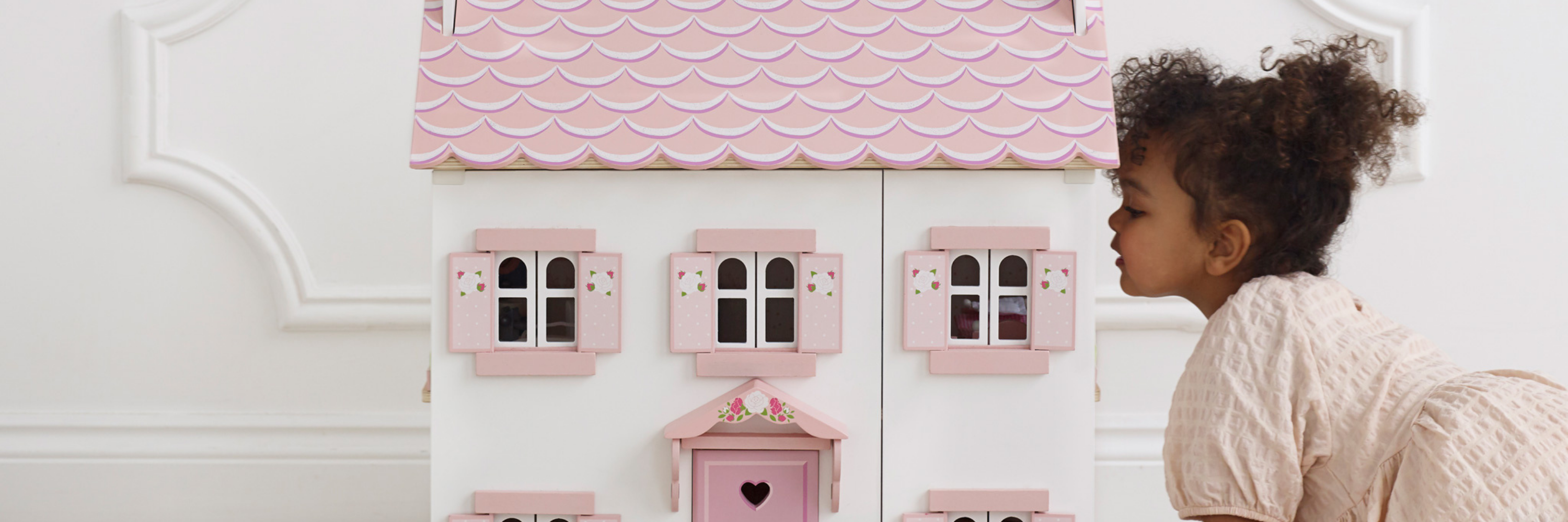 Child looking at a pink toy house with a white wall background