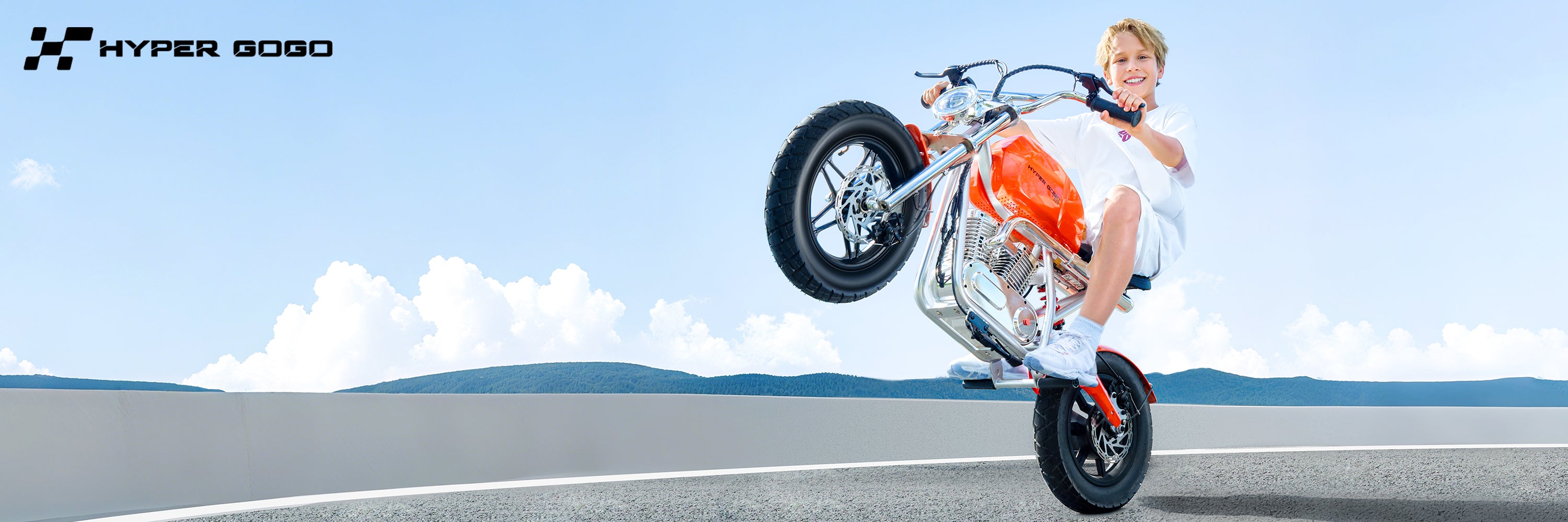 Person performing a wheelie on a Hyper GoGo electric bike with a clear blue sky and road in the background.