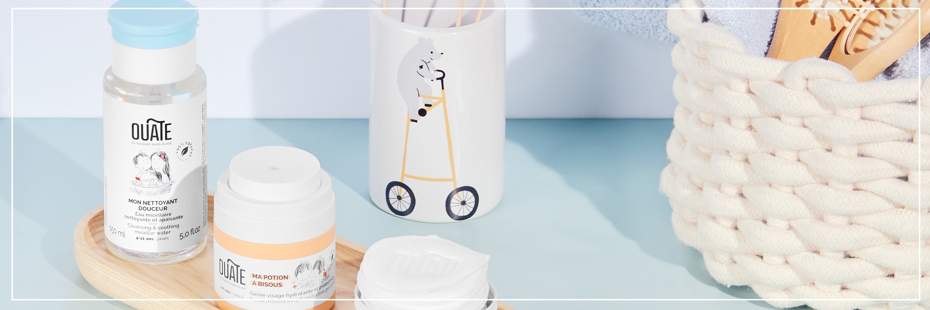 Cosmetic products including bottles and a jar on a light blue surface with a white basket in the background.