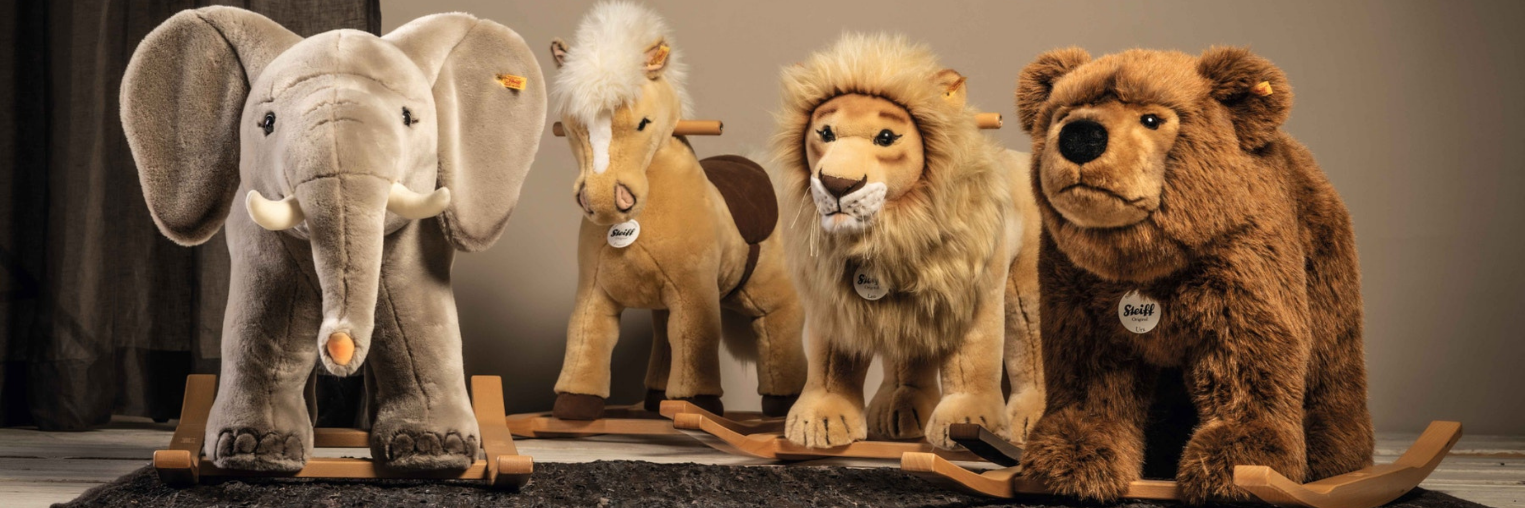 Four stuffed animals (elephant, horse, lion, bear) standing on a wooden platform against a neutral background.