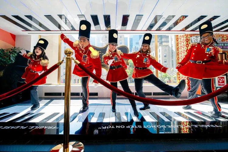 Costumed performers in red outfits and black hats on a piano stage with a cityscape background