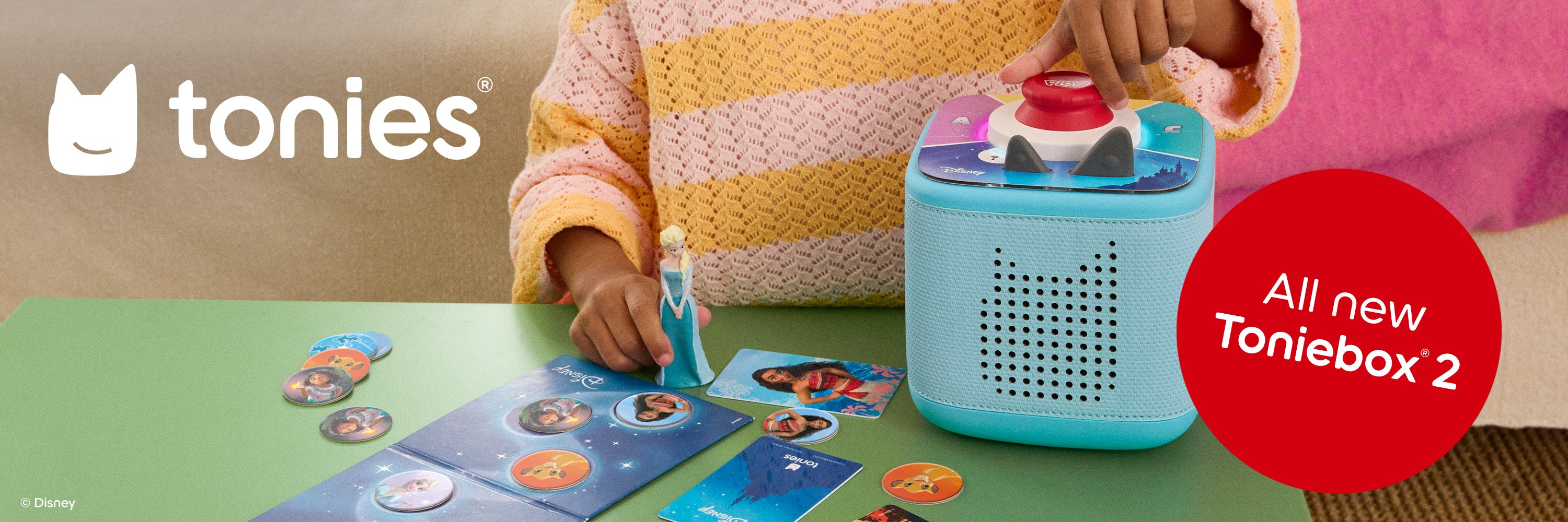 Person interacting with a Toniebox 2 toy on a green surface with colorful cards.