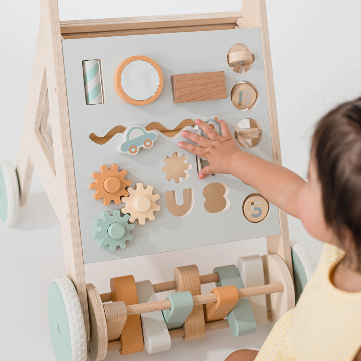 baby playing with wooden activity walker toy neutral colors