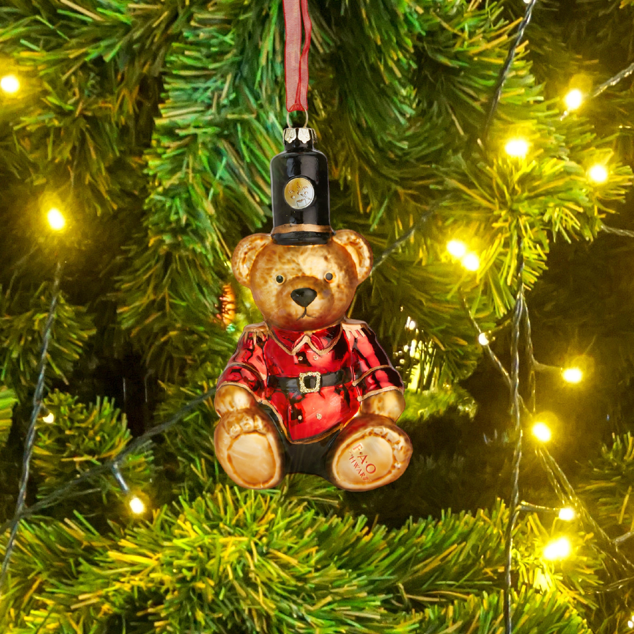 Decorative teddy bear ornament with a top hat hanging on a Christmas tree.