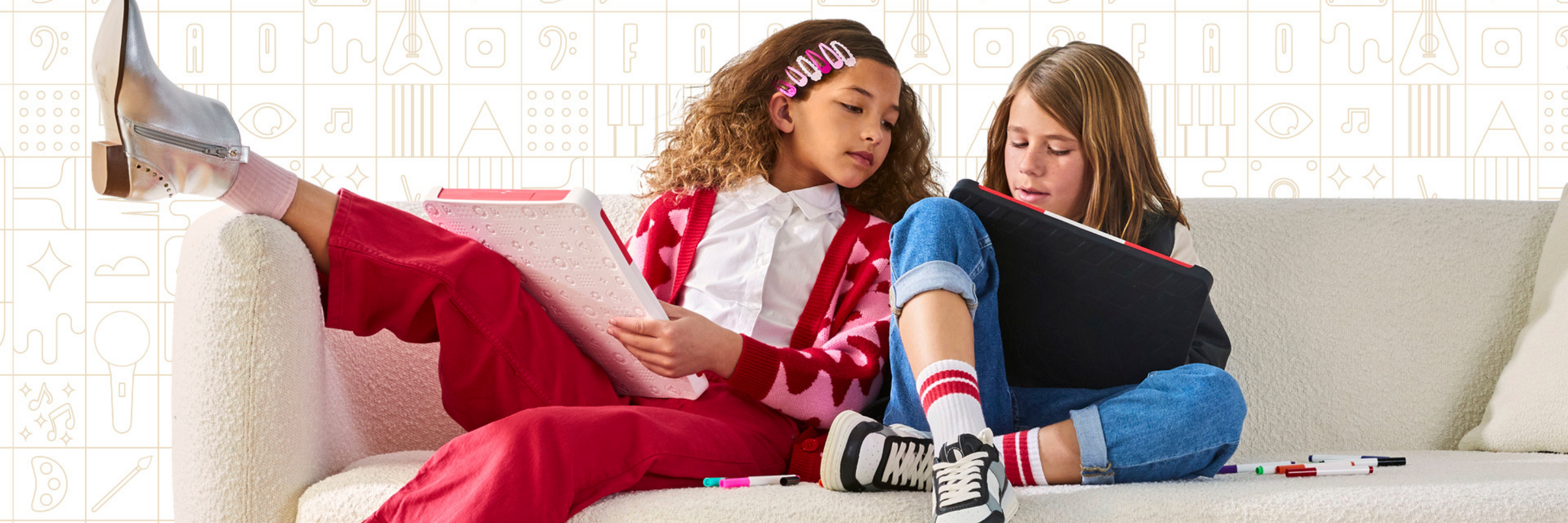 Two children sitting on a couch, reading books with colorful markers around them.