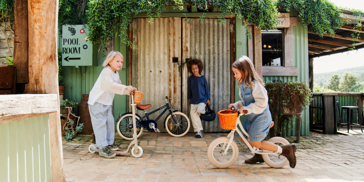 Children playing with bicycles and scooters in a rustic outdoor setting.