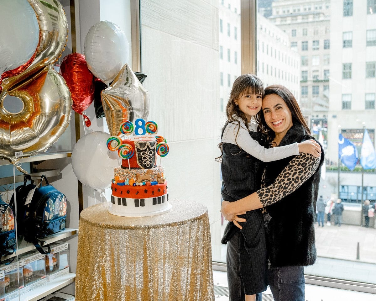 a woman and child hugging next to a three tiered cake with balloons