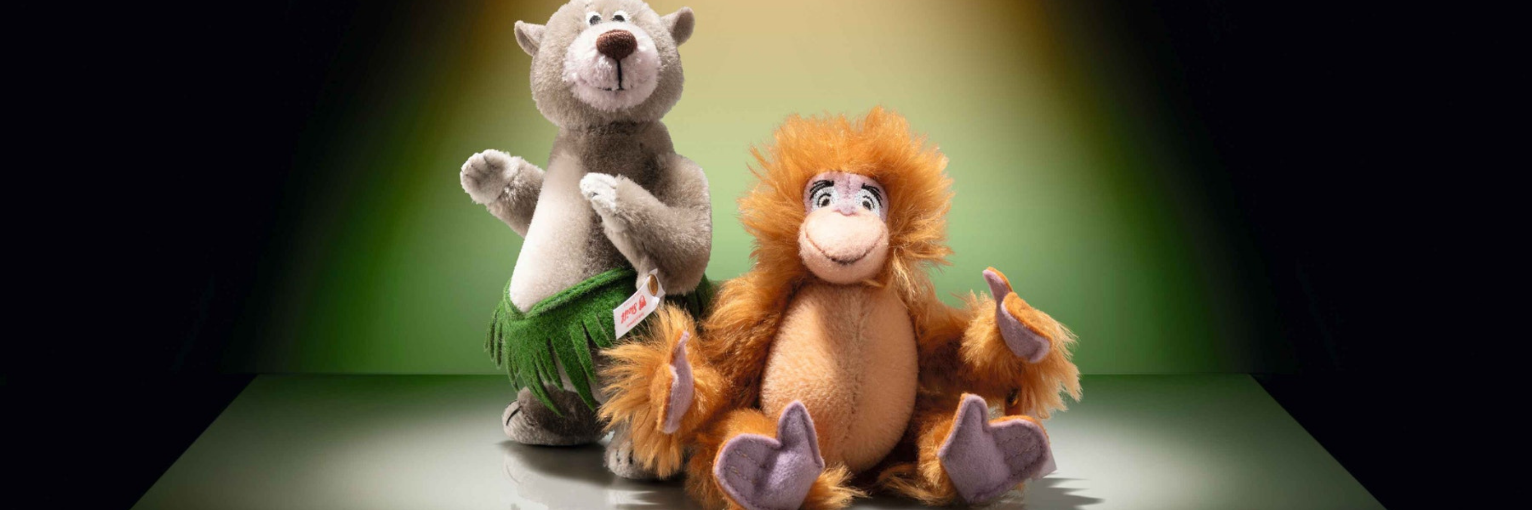 Two plush toys, a bear and a lion, on a dark background with a spotlight effect.