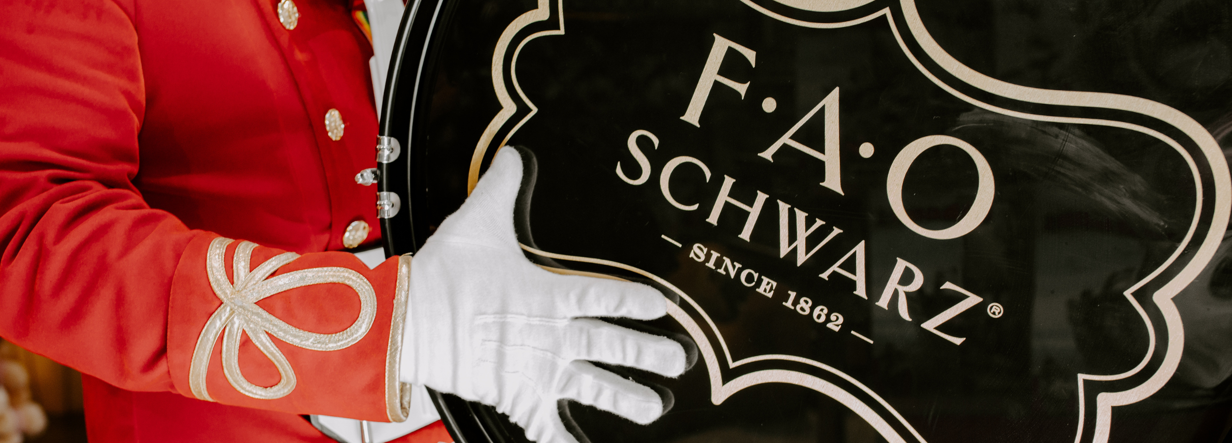 Person in red uniform with white gloves holding a F.A.O. Schwarz sign.