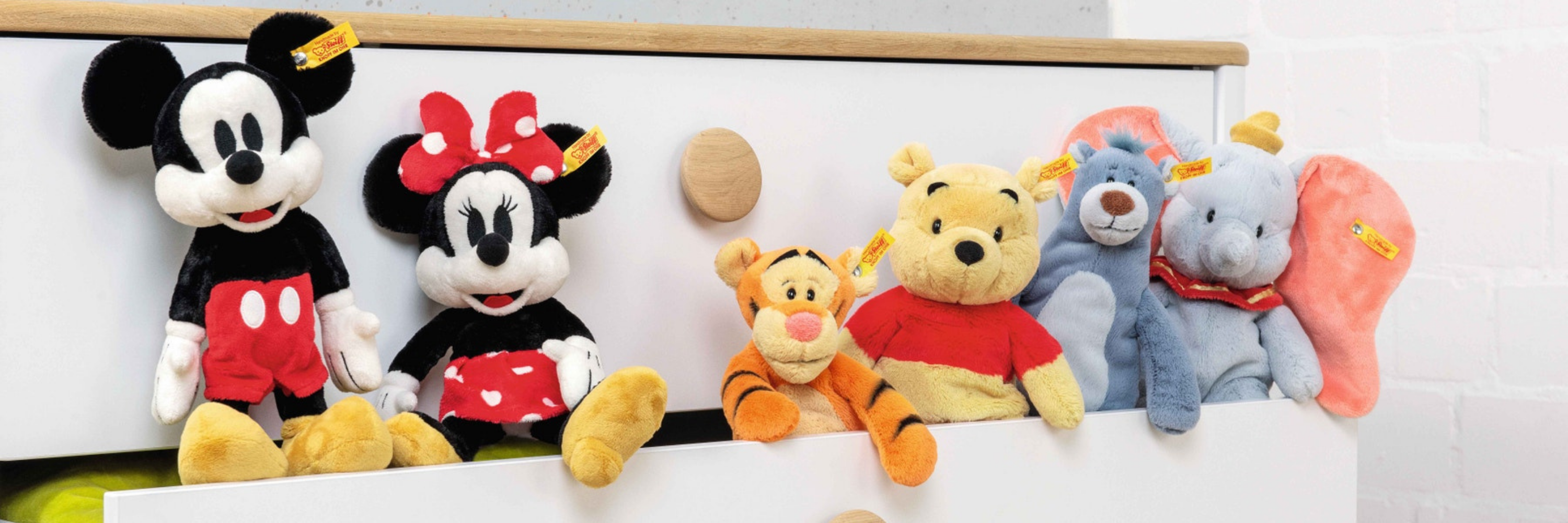Collection of colorful plush toys including Mickey Mouse, Minnie Mouse, and Winnie the Pooh on a white surface.