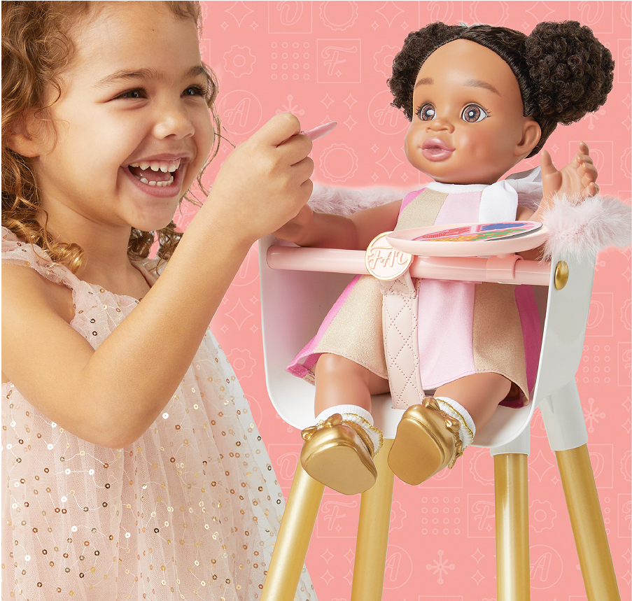 Child playing with a doll in a high chair against a pink background