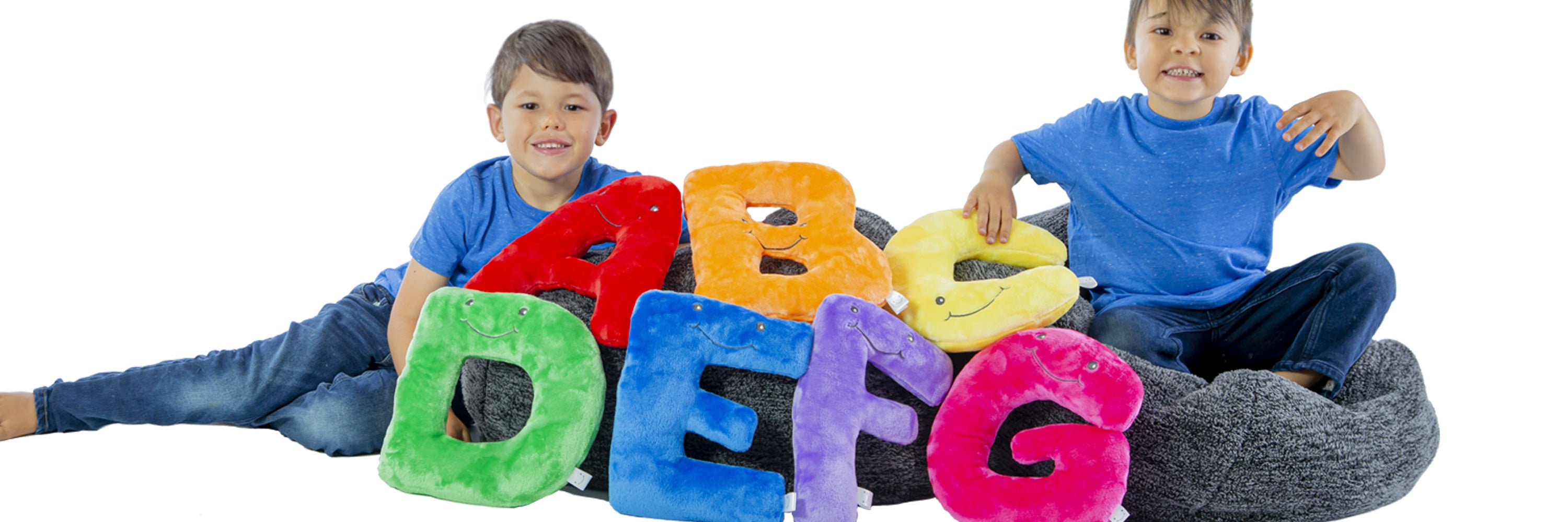 Two children sitting on a bean bag with colorful letters spelling 'ABC' on a white background