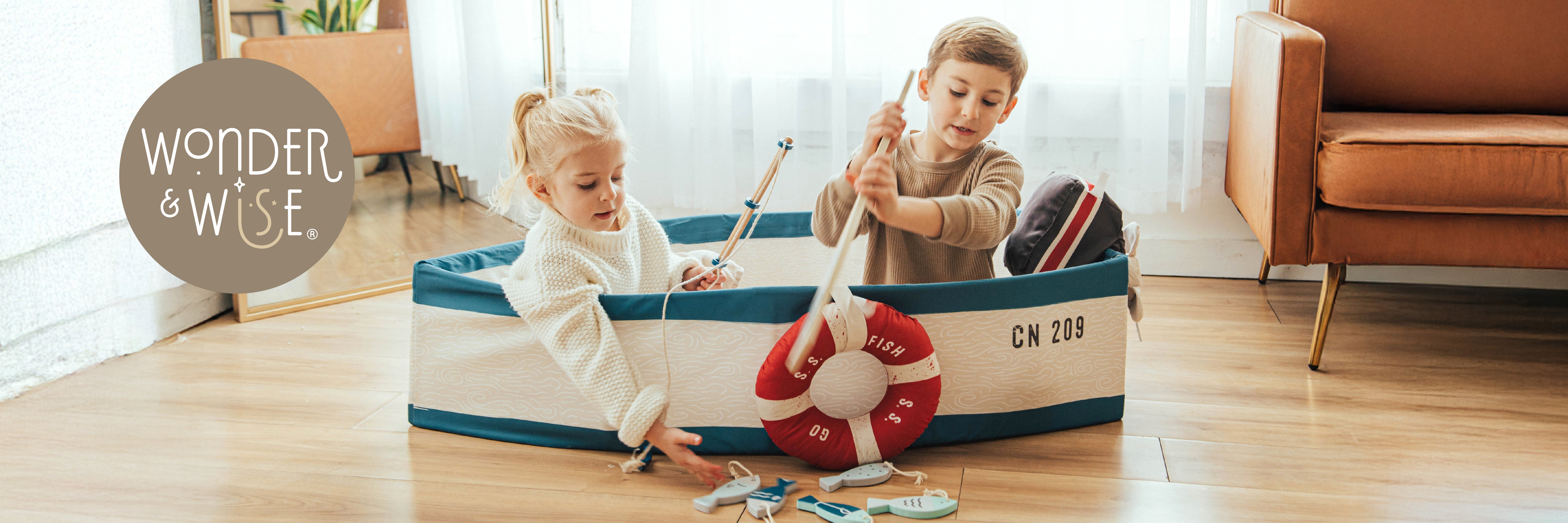 Two children playing with a toy boat in a large toy box labeled 'Wonder & Wise' in a home setting.
