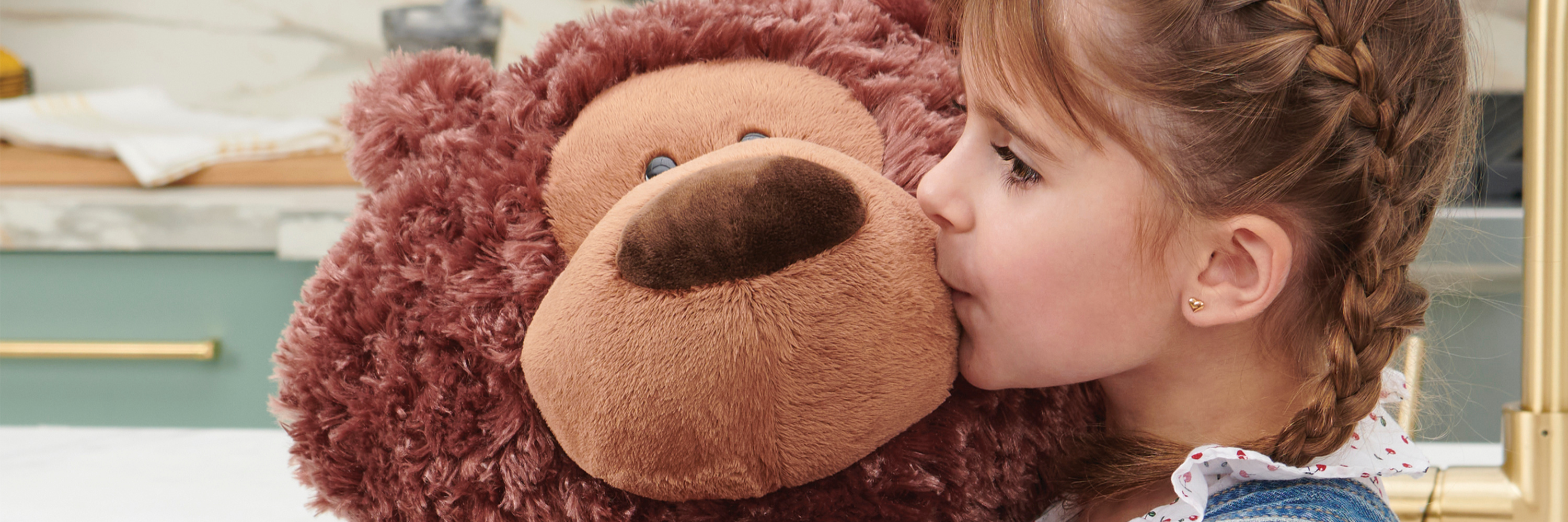 Child kissing a large brown teddy bear with a blurred background