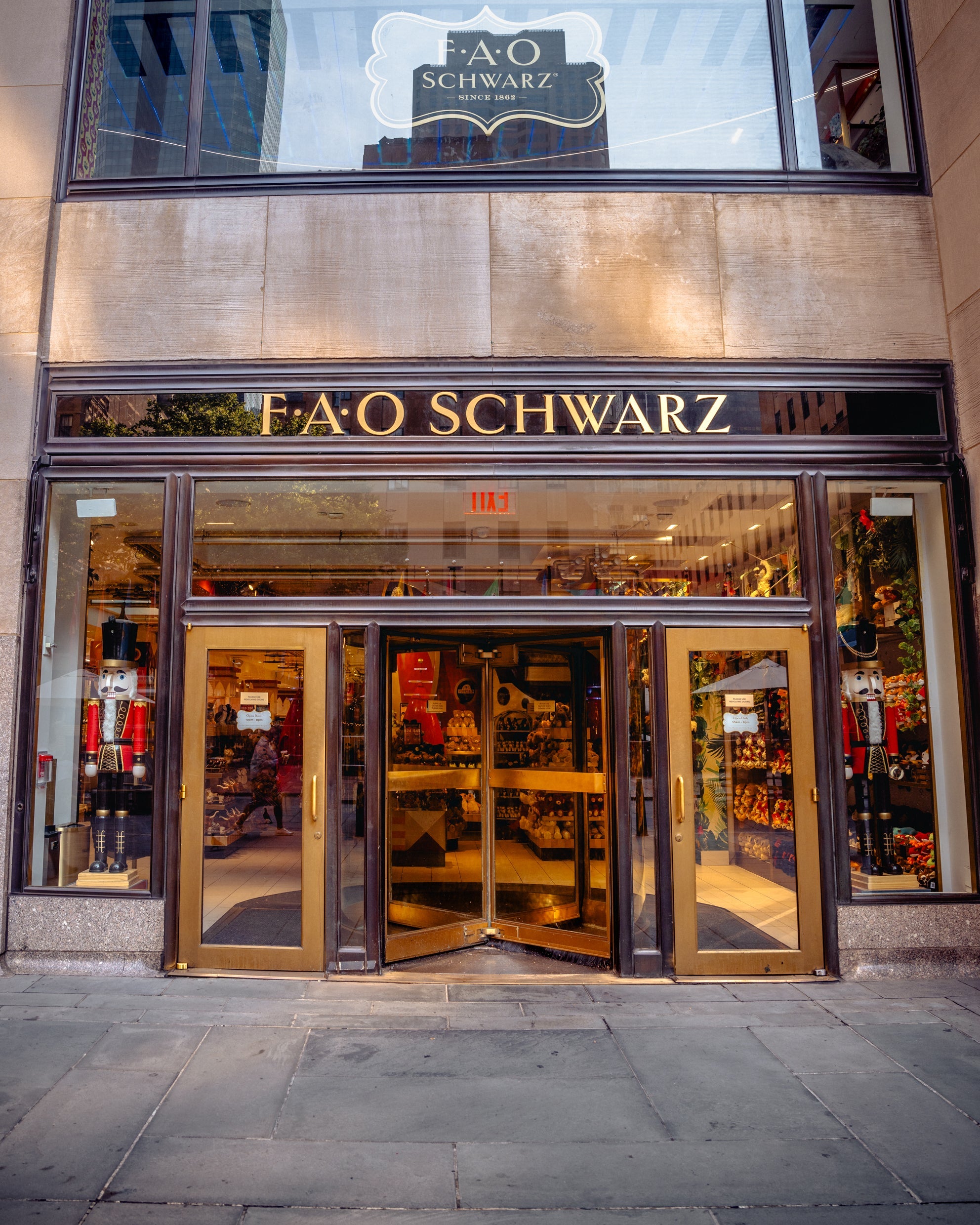 FAO Schwarz store entrance with gold doors and sign on a city street.