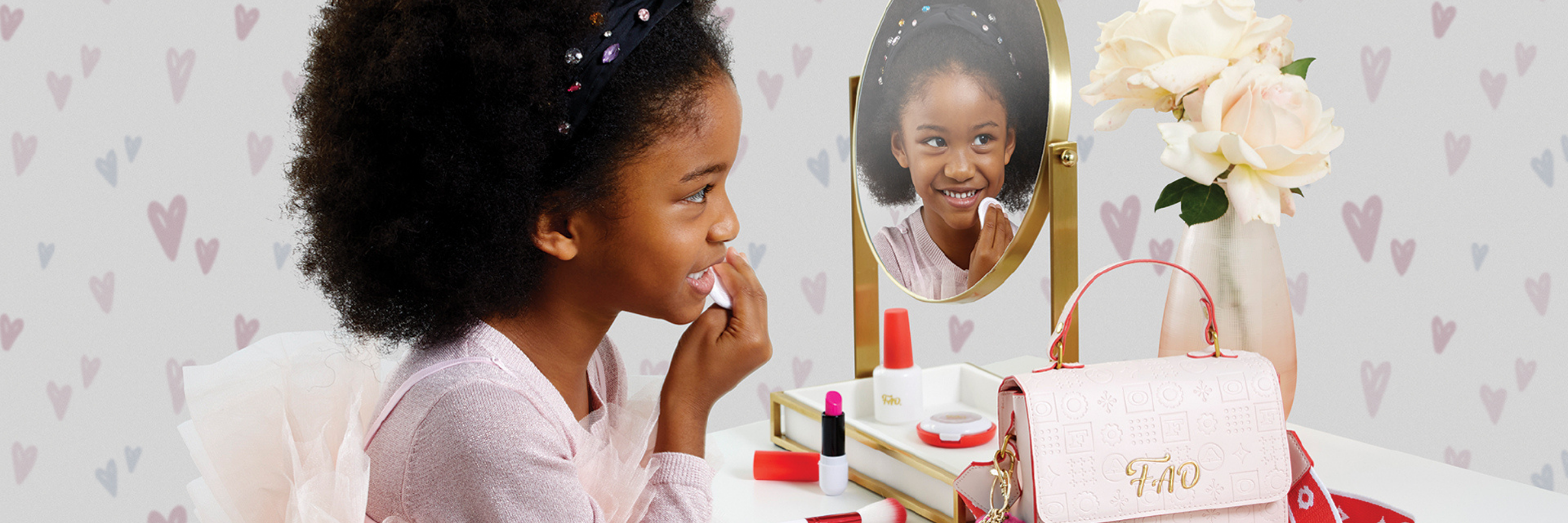 Young girl applying makeup in front of a mirror with a heart-patterned wall.