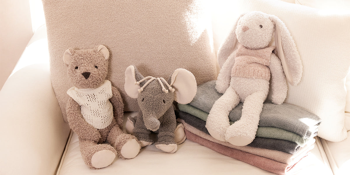 Three plush toys including a bear, elephant, and rabbit sitting on a stack of folded blankets.