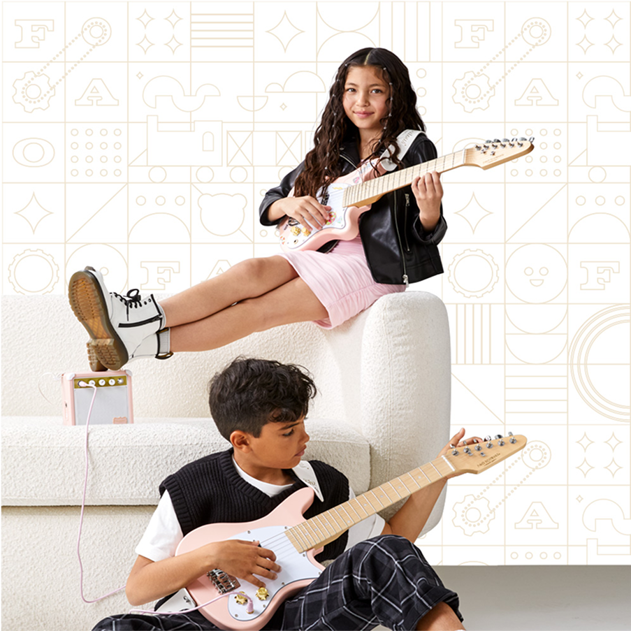 Two children playing electric guitars on a white couch with a geometric patterned wall in the background.