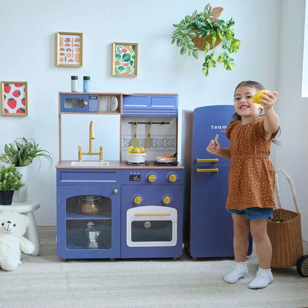 Child playing with a toy kitchen set in a room with decor elements.
