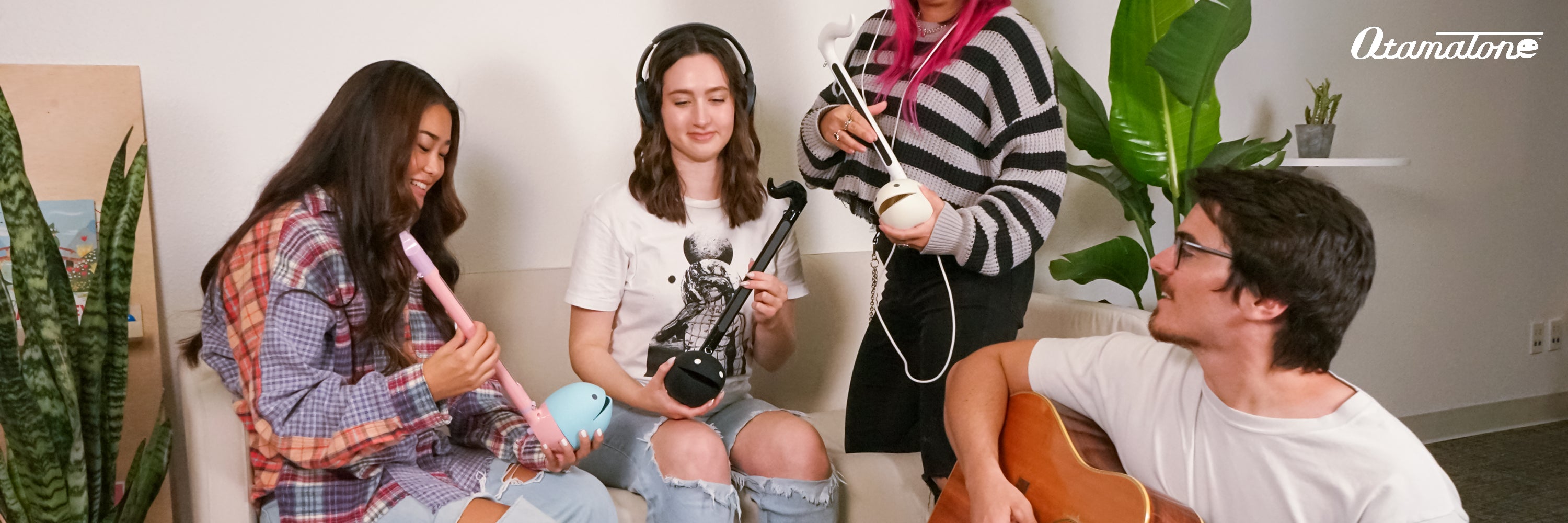 Four young people sitting on a couch with musical instruments in a casual indoor setting.