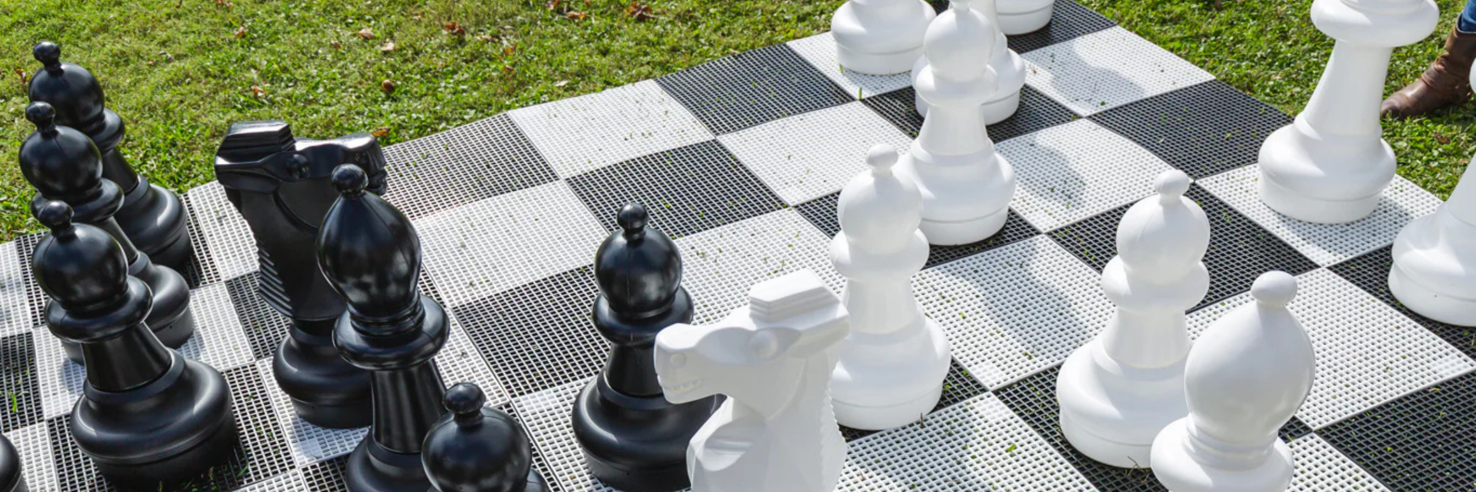 Large outdoor chess set with black and white pieces on a checkered surface.