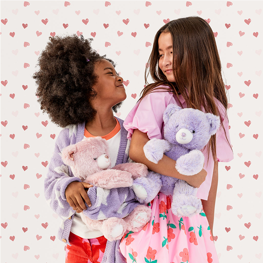 Two children holding teddy bears against a heart-patterned background