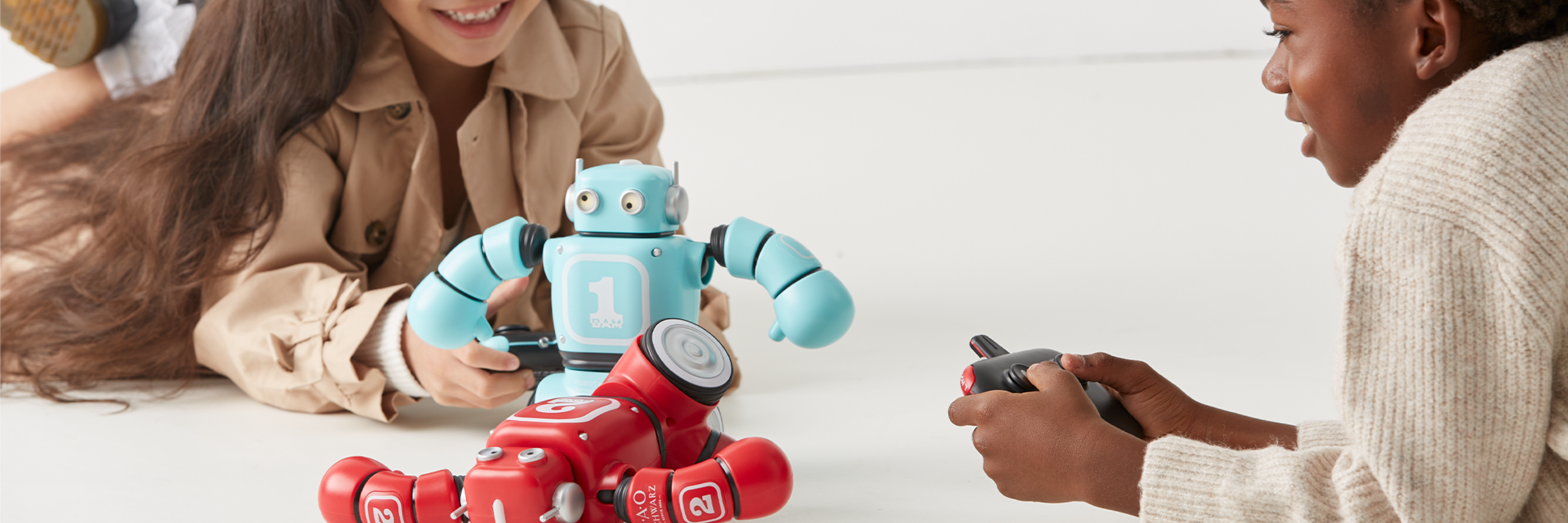 Two people interacting with a robot toy on a white surface