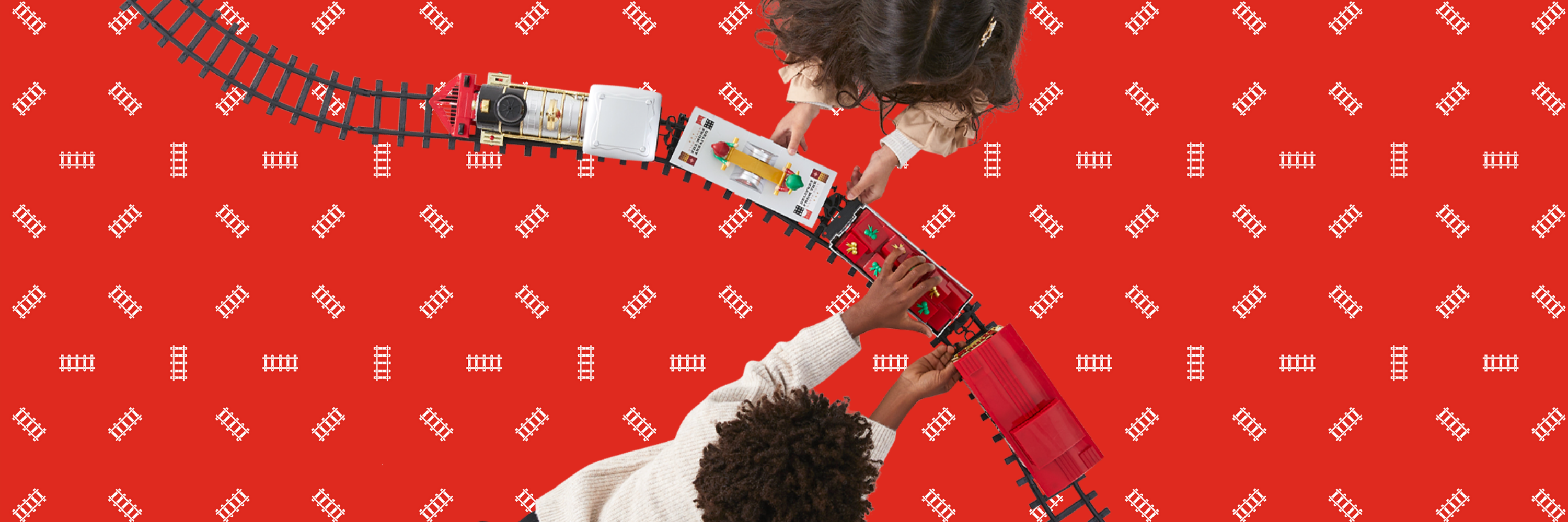 Two children playing with a toy train set against a red background with a subtle pattern.