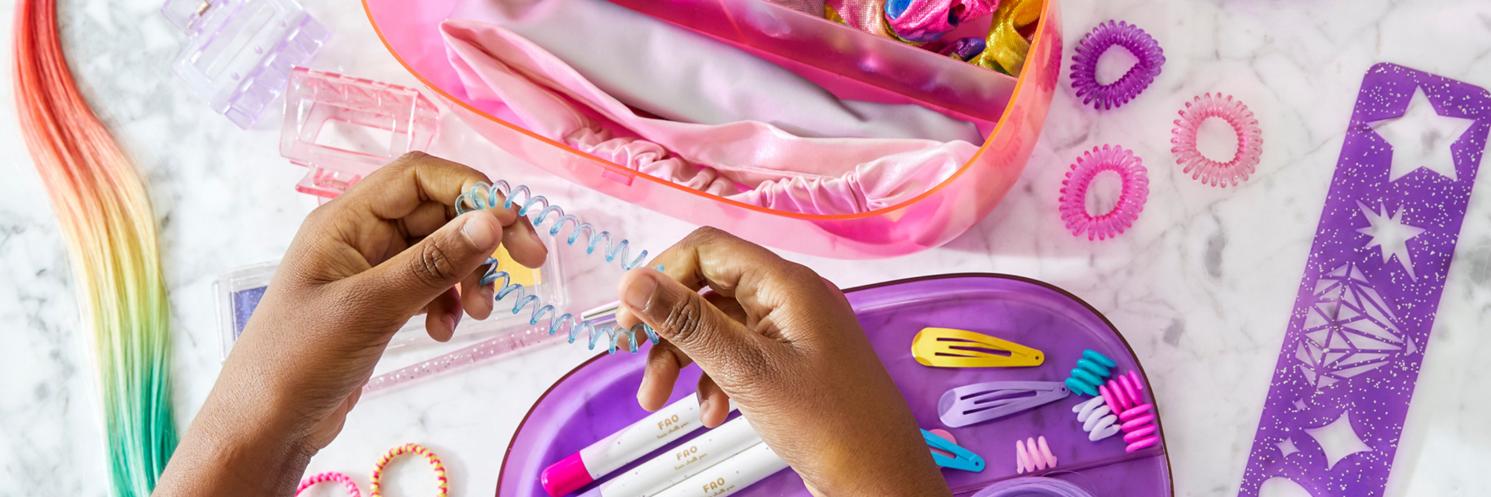 Children's hands using a hair styling tool with colorful accessories on a white surface