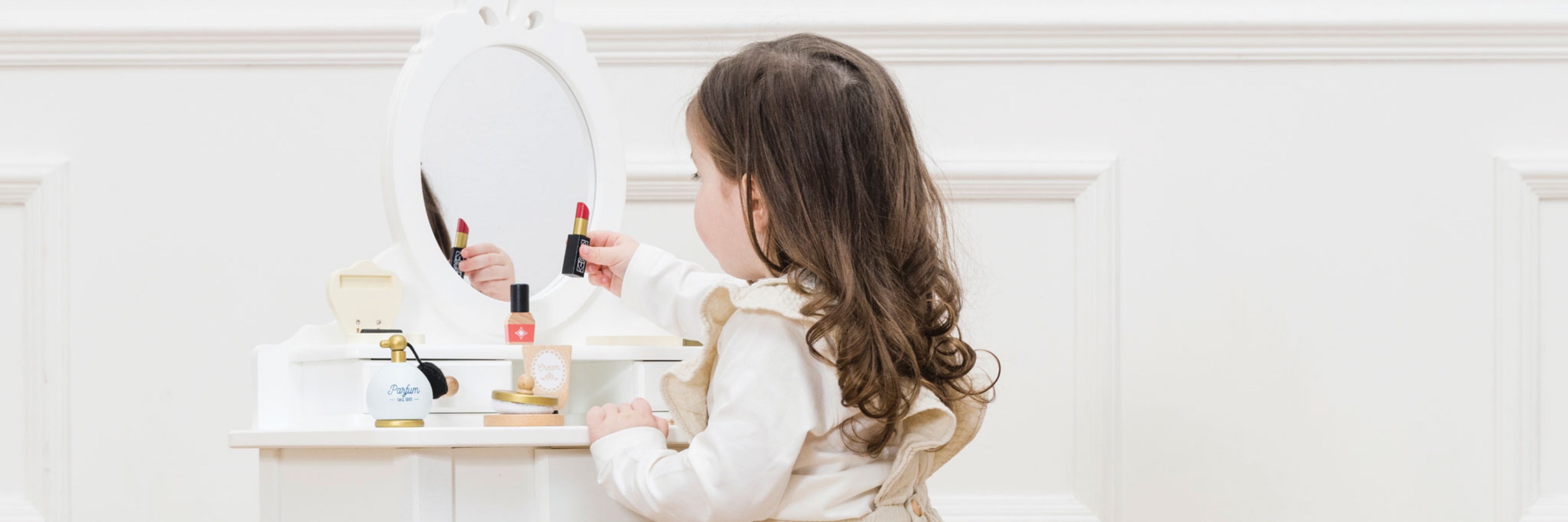 Young girl playing with makeup products in front of a mirror.