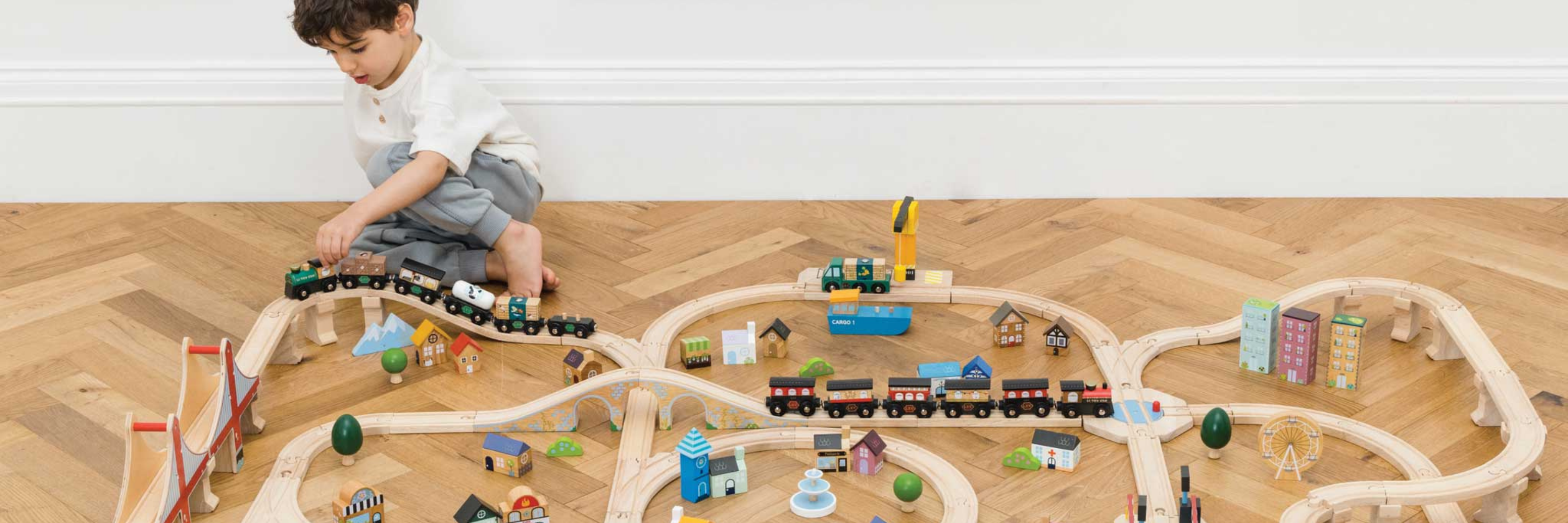 Child playing with a toy train set on a wooden floor