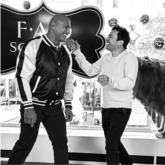 Two men laughing in a room with a large logo on the wall.