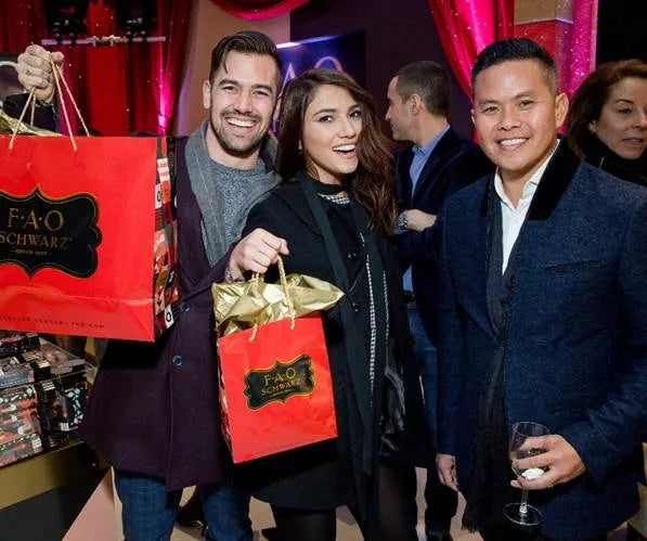 People holding FAO Schwarz shopping bags in a festive indoor setting